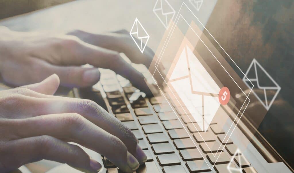Close-up of hands typing on a laptop keyboard with a digital overlay of email icons. A glowing envelope with a red notification badge indicating five unread messages appears, symbolizing email communication and inbox management. The image blends real and digital elements, emphasizing technology and online correspondence.