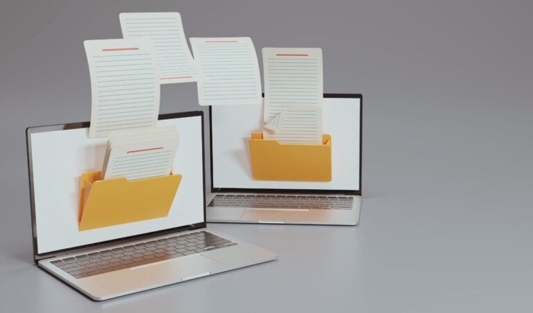 A conceptual 3D-rendered image of two laptops with yellow file folders displayed on their screens. Digital documents appear to be flying between the two devices, symbolizing file transfer, digital organization, or data sharing. The background is neutral gray, emphasizing the technology-focused theme